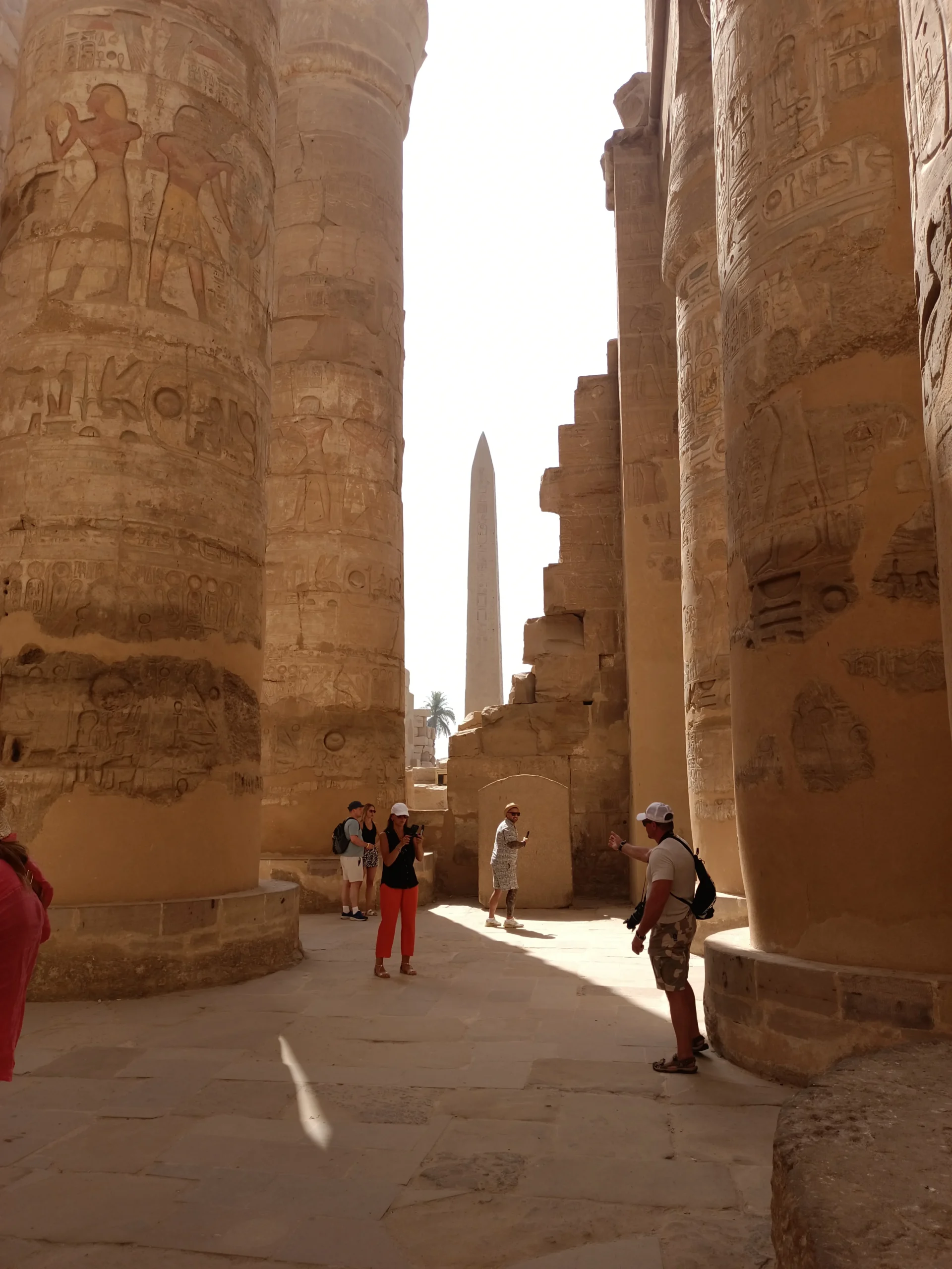 Große Säulen mit Hieroglyphen in der Säulenhalle des Karnak-Tempels, im Hintergrund ein Obelisk, Luxor, Ägypten.
