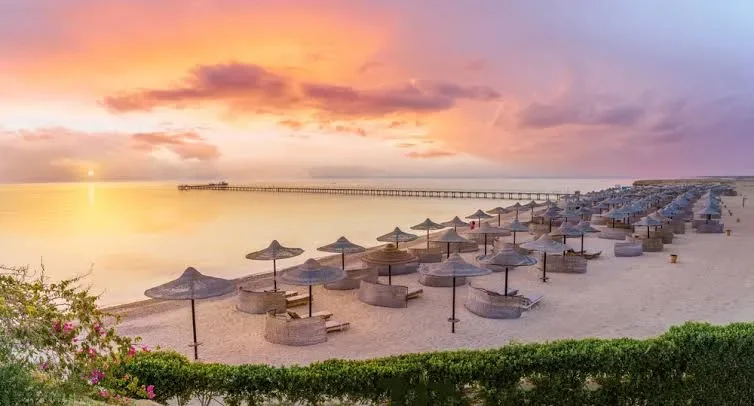 Sonnenuntergang &uuml;ber dem Strand von Hurghada mit Strohschirmen und Liegest&uuml;hlen am Roten Meer