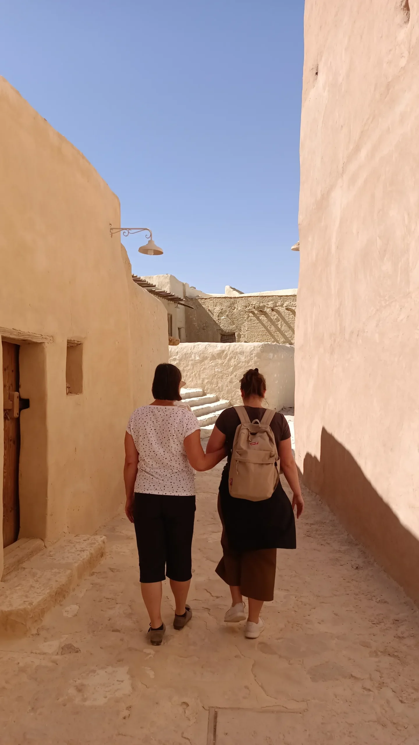 Zwei Frauen spazieren durch eine enge Gasse mit Lehmhäusern in einem historischen ägyptischen Oasendorf.