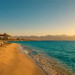 Sonnenliegen und Palmen am t&uuml;rkisfarbenen Strand von Hurghada bei Sonnenuntergang.
