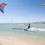 Kitesurfer im t&uuml;rkisfarbenen Wasser vor Hurghada mit zahlreichen Kites am Himmel.