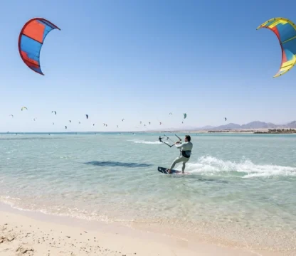 Kitesurfer im t&uuml;rkisfarbenen Wasser vor Hurghada mit zahlreichen Kites am Himmel.
