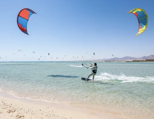 Kitesurfer im t&uuml;rkisfarbenen Wasser vor Hurghada mit zahlreichen Kites am Himmel.