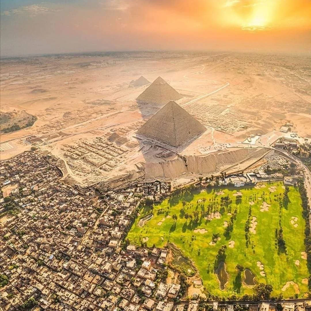 Luftaufnahme der Pyramiden von Gizeh bei Sonnenuntergang zwischen Wüste und Stadt Kairo.