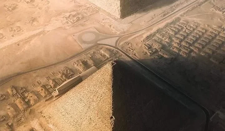 Luftaufnahme der Pyramiden von Gizeh mit angrenzender Wüstenlandschaft und Straßen bei Sonnenuntergang.